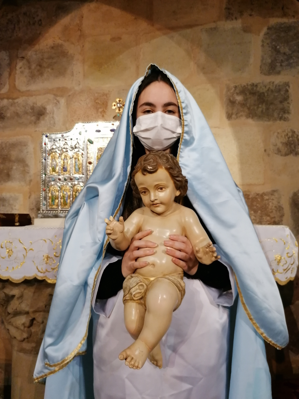 La Virgen María con mascarilla, sosteniendo en sus brazos al Niño Jesús